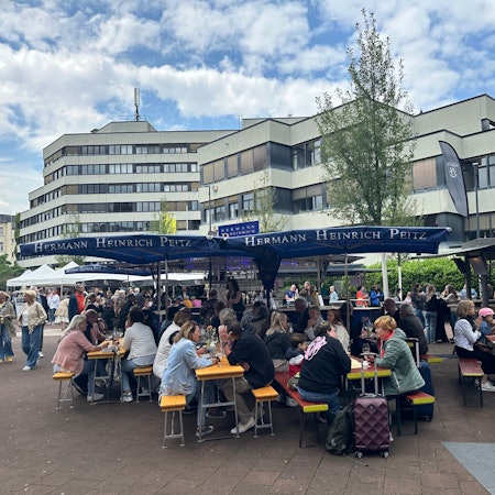 Menschen sitzen beim Weinfest in Siegburg auf Bierbänken.