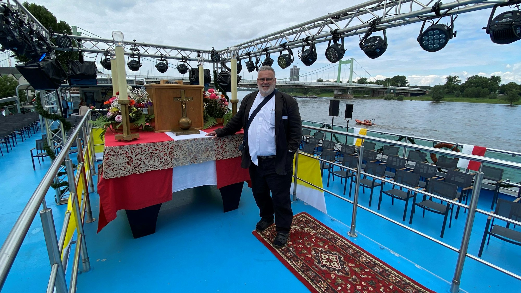 Pfarrer Bruno Nebel steht auf der MS RheinFantasie vor der Schiffprozession der Mülheimer Gottestracht in Köln.