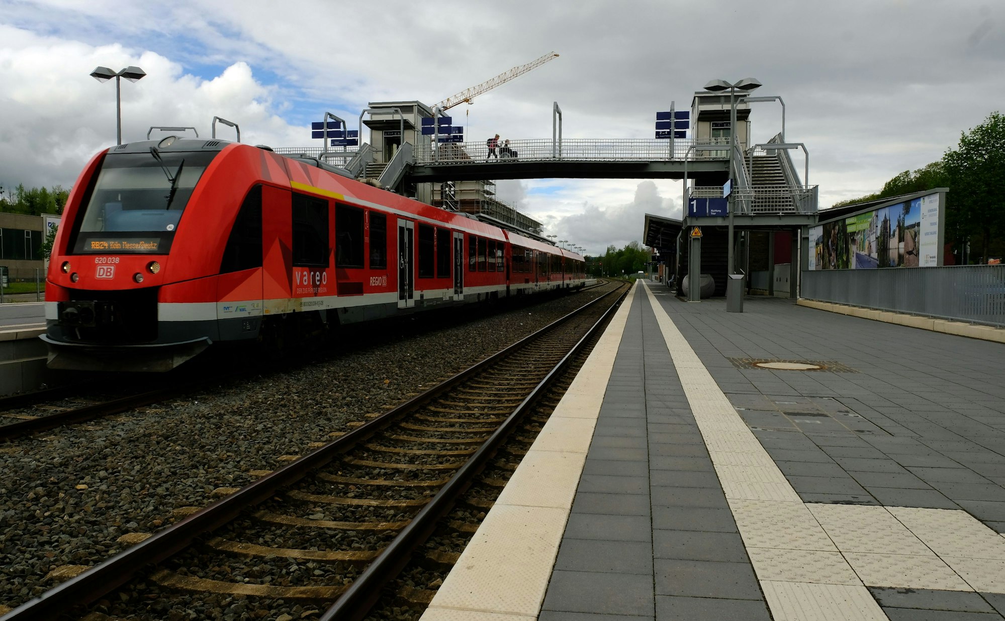 Die Fußgängerbrücke am Bahnhof Mechernich ist zu sehen. Ein roter Zug steht auf den Gleisen.