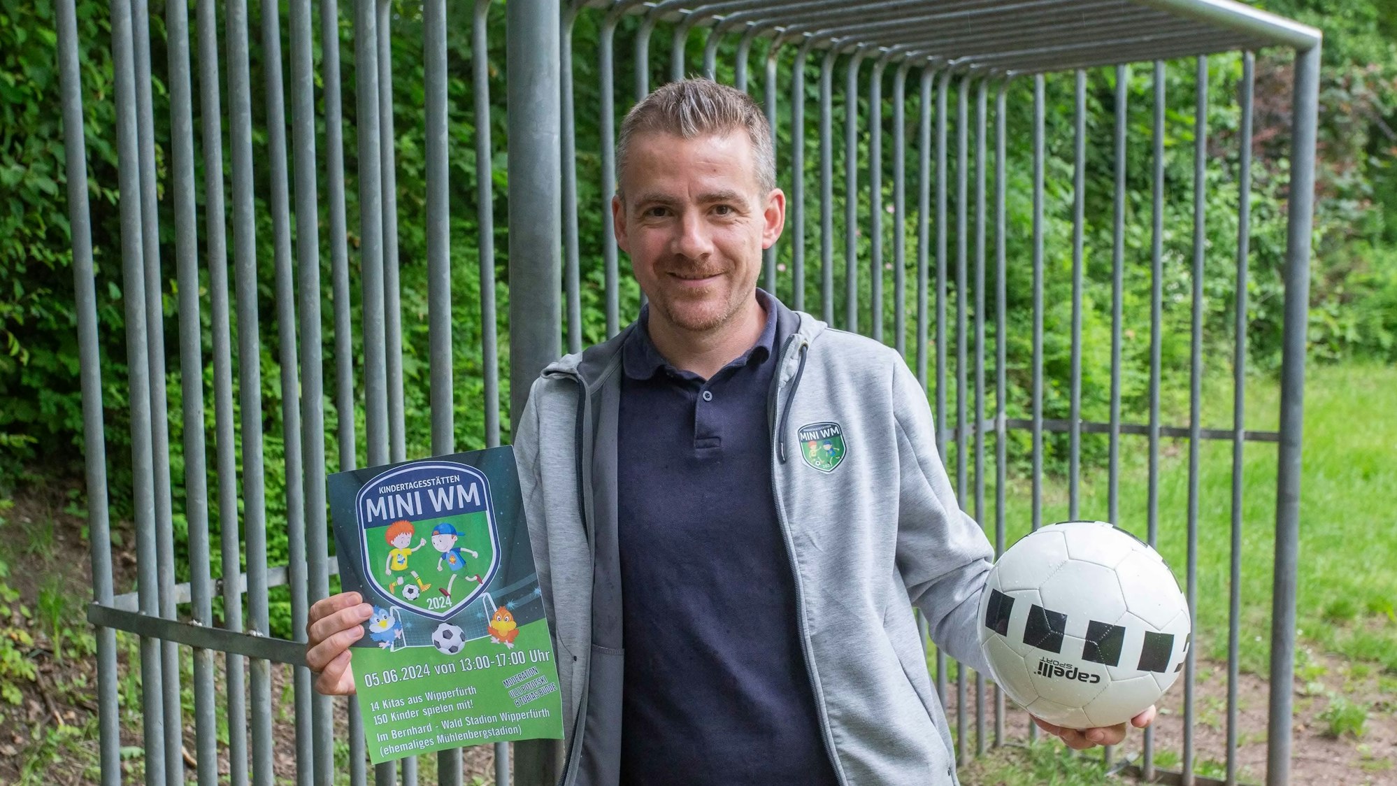Mit Flyer und Ball in den Händen steht Dominic Willms vor einem Fußballtor.