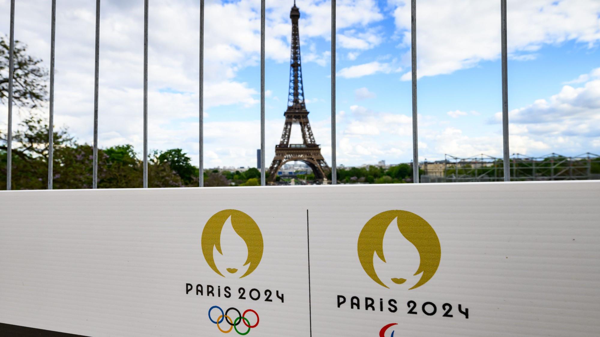 Die Olympischen Ringe und das Logo der Paralympischen Spiele sind auf einem Schild an einem Bauzaun vor dem Eiffelturm zu sehen. (Archivbild)