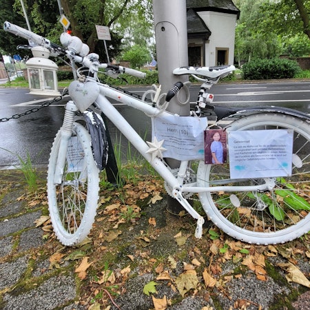 Ein weiß lackiertes Fahrrad ist an einem Laternenmast befestigt.