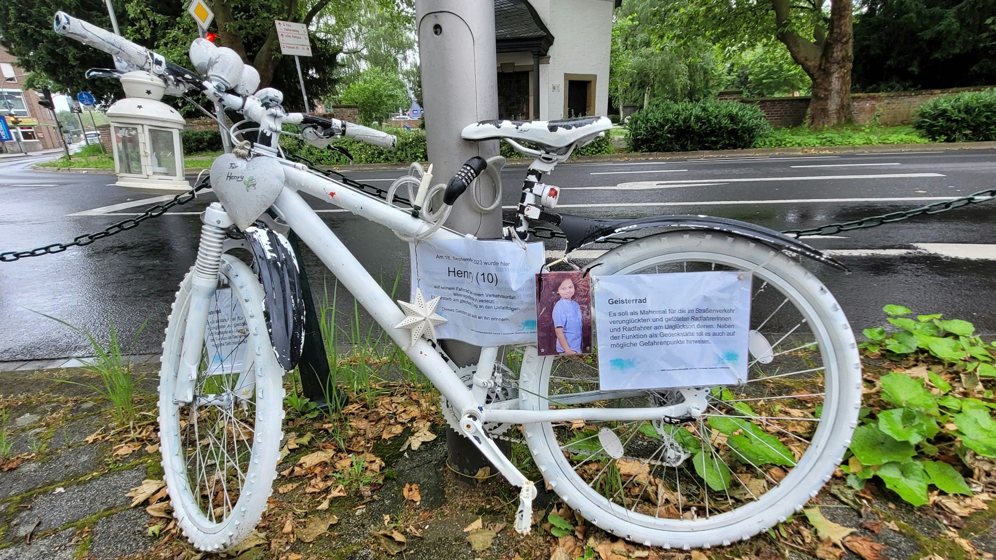 Ein weißes Fahrrad, Geisterfahrrad genannt, lehnt an einer Straßenlaterne.