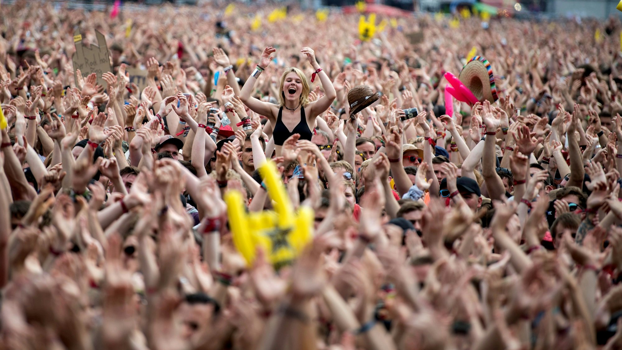 Das Bild zeigt die Fans vor der Hauptbühne des Festivals. Eine Frau sitzt auf den Schultern eines Fans und klatscht in die Hände.