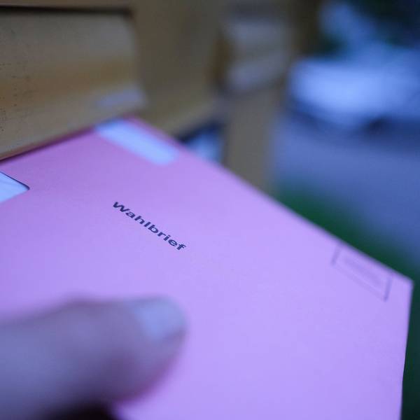 Eine Hand hält an einem Briefkasten einen Wahlbrief für die Stimmzettel der Wahlen für das Europaparlament.