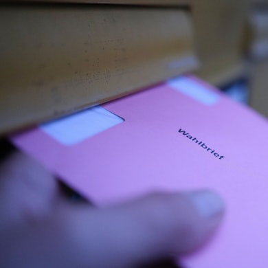 Eine Hand hält an einem Briefkasten einen Wahlbrief für die Stimmzettel der Wahlen für das Europaparlament.