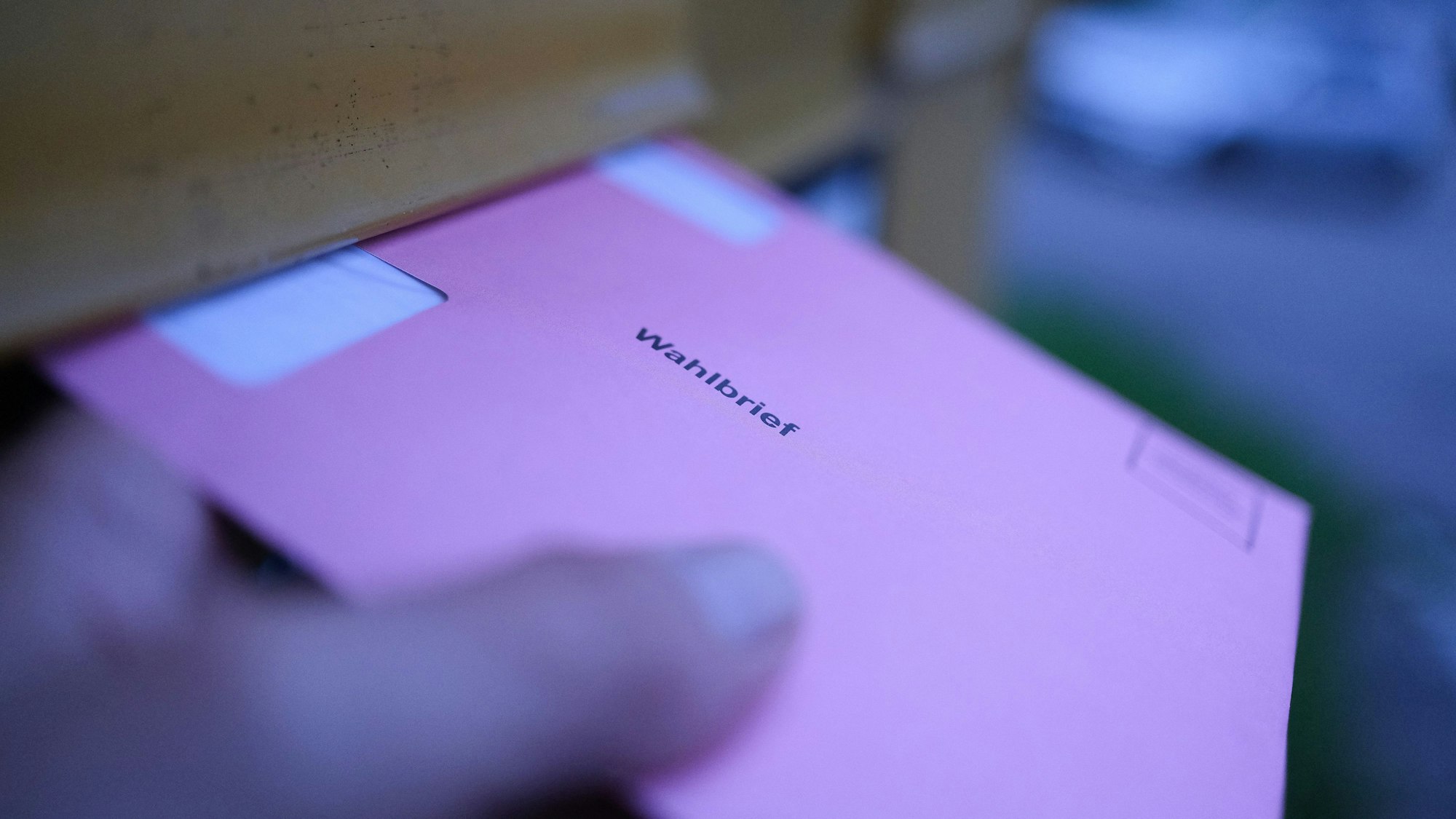 Eine Hand hält an einem Briefkasten einen Wahlbrief für die Stimmzettel der Wahlen für das Europaparlament.