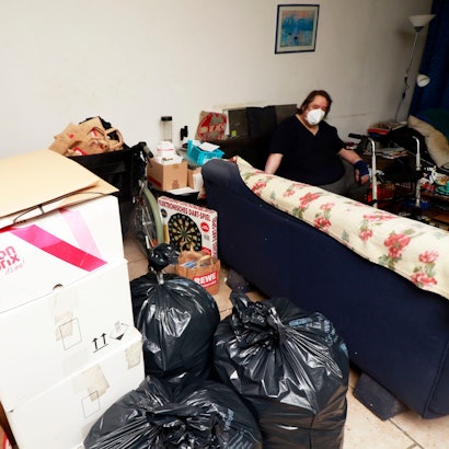 Köln: Müllsäcke und Packete prägen das Bild in dieser Wohnung. Ein Pflegebedürftiges Paar lebt in unwürdigen Zuständen und bekommt keine Hilfe von der Stadt und Pflegedienste. Zu sehen sind Müllsäcke und Umzugskartons, ein Mann mit Maske sitzt auf dem Sofa und stützt sich auf einen Rollator.