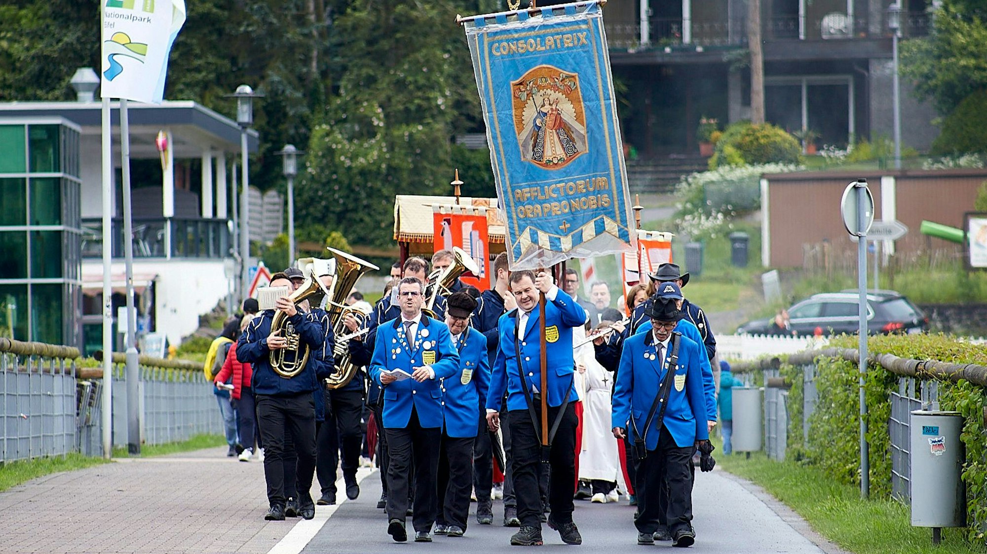 Die Fronleichnams-Prozession in Rurberg wird von der Kevelaer-Bruderschaft angeführt. Die Männer tragen blaue Jacketts, einer hält eine Fahne in die Höhe.