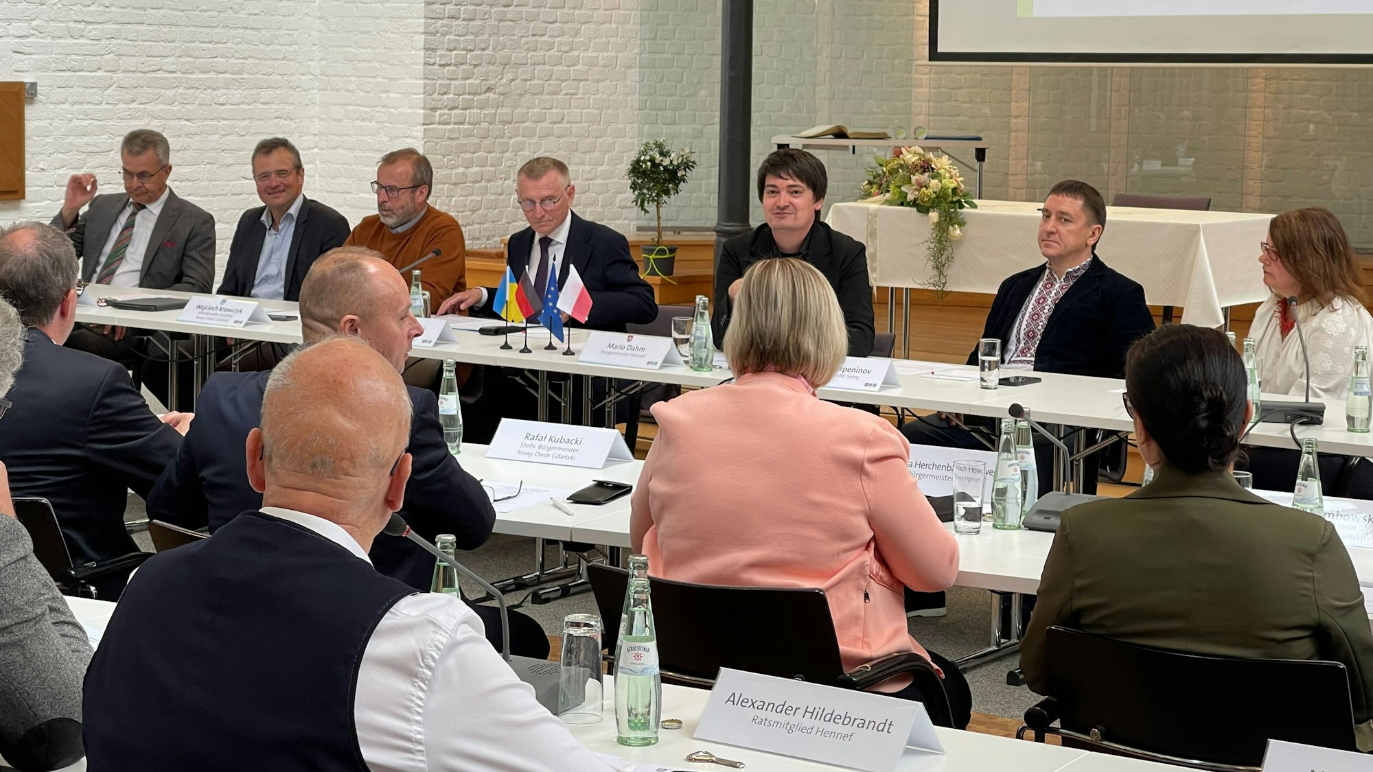 Menschen sitzen an hintereinander aufgestellten Tischreihen.