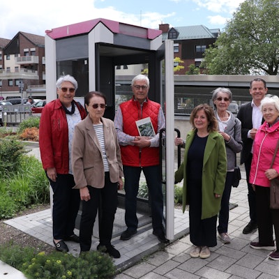 Sieben Personen stehen an einer alten, instand gesetzten Telefonzelle.