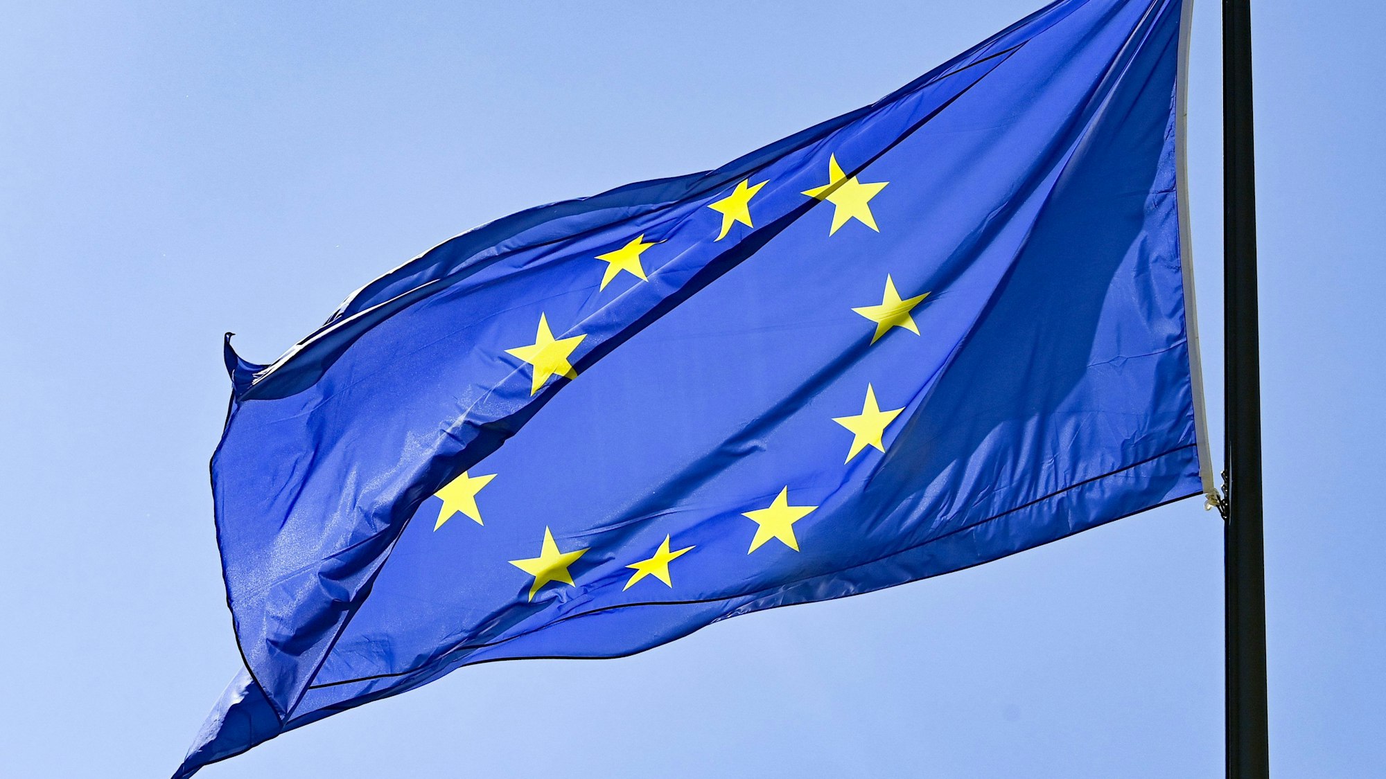 Eine Europaflagge weht vor blauem Himmel.