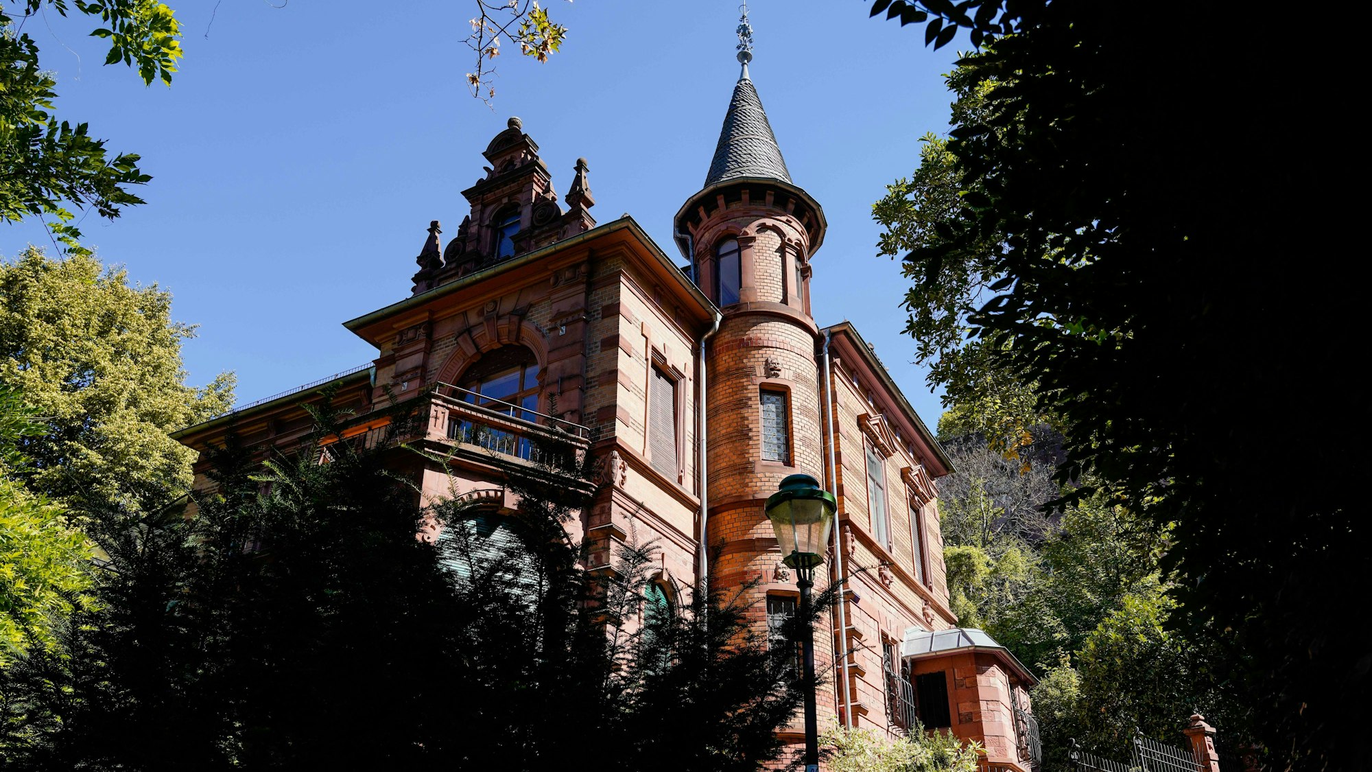 Blick auf das Haus der Burschenschaft Normannia. Eine Villa in Renaissance-Backsteinbauweise ist zu sehen mit Türmichen und Erker. Davor Bäume und Sträucher.