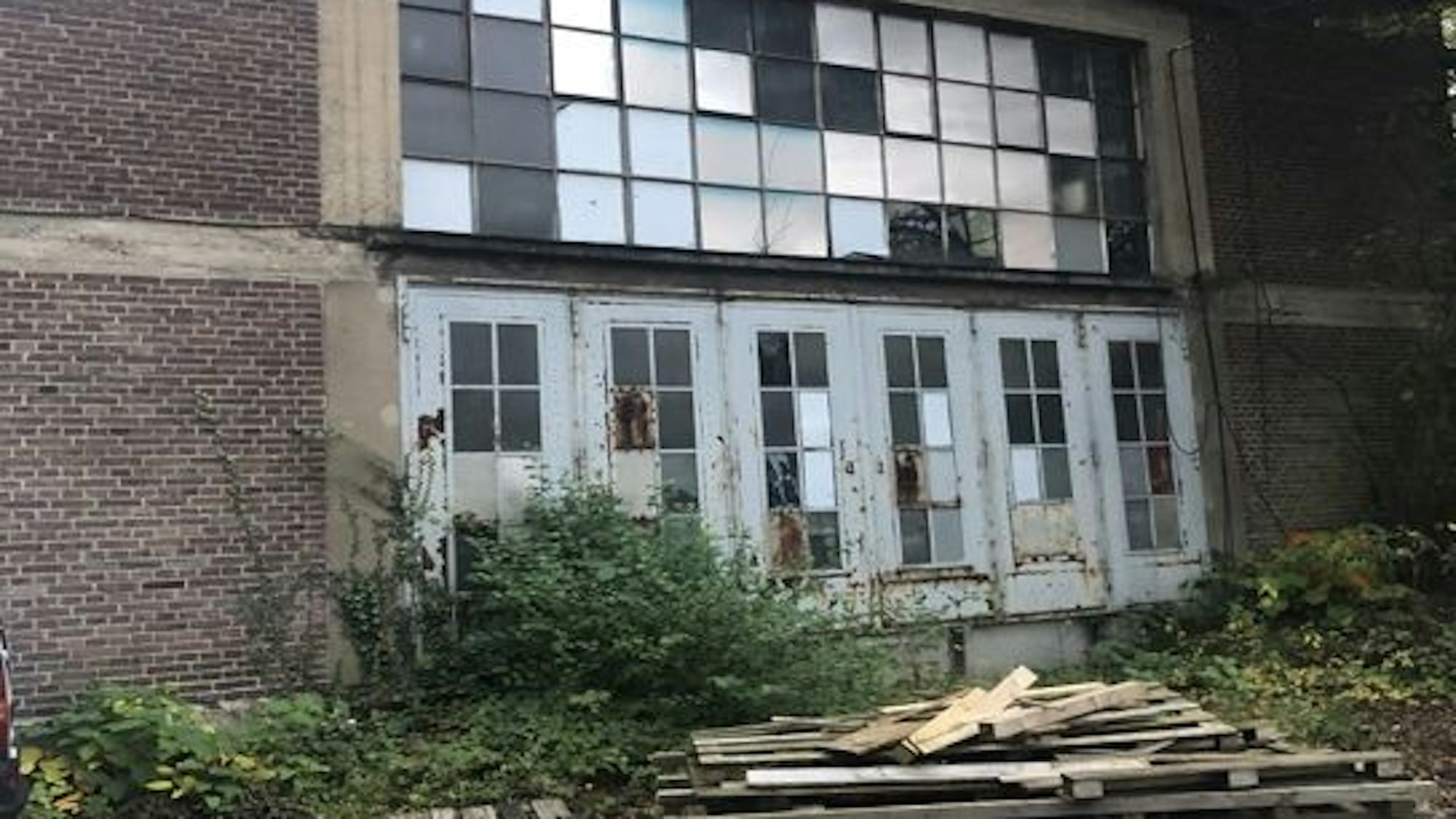 Runtergekommene Gebäudefront eines Ziegelbaus. Davor liegen Holzlatten gestapelt.