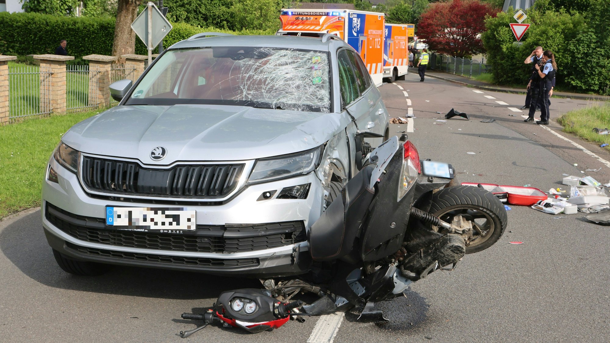 Ein Bild nach einem schweren Verkehrsunfall zwischen einem Roller- und einem Autofahrer. Das Vorderrad des Rollers ist unter der linksseitigen Frontpartie des Autos eingeklemmt.