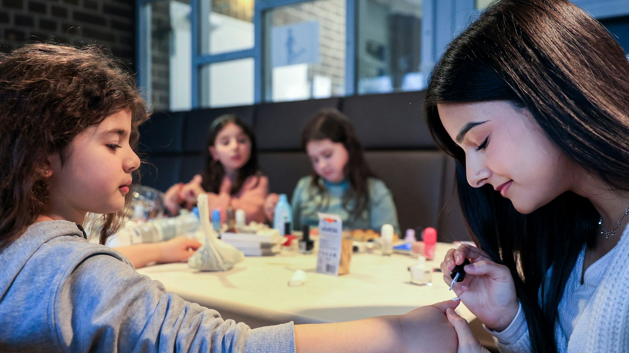 Die Leiterin des „Mädchenkram“-Nachmittags Meera Kalra (rechts) lackiert einer jungen Teilnehmerin die Nägel