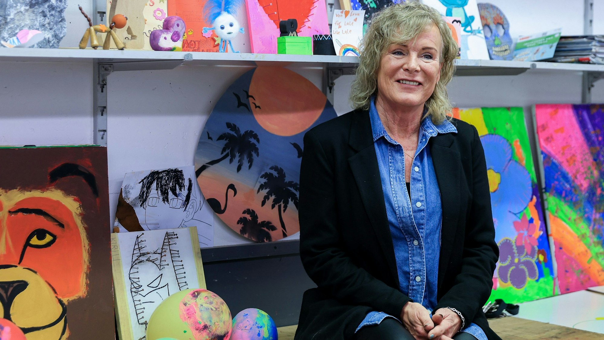 Die Leiterin des Jugendzentrums Glashütte, Petra Riemann, sitzt im Kunstatelier der Porzer Einrichtung vor vielen knallbunten Gemälden.