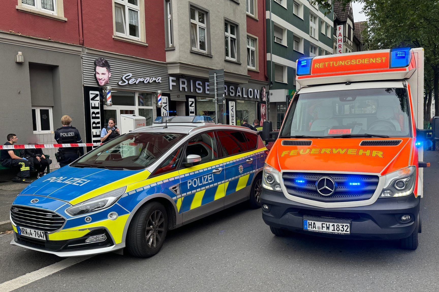 Ein Einsatzfahrzeug der Polizei und ein Rettungswagen der Feuerwehr stehen vor einem Friseursalon.