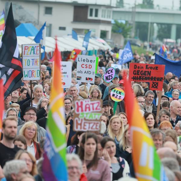 Menschen demonstrieren mit Plakaten und Regenbogen- oder Europaflaggen.