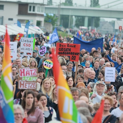 Menschen demonstrieren mit Plakaten und Regenbogen- oder Europaflaggen.