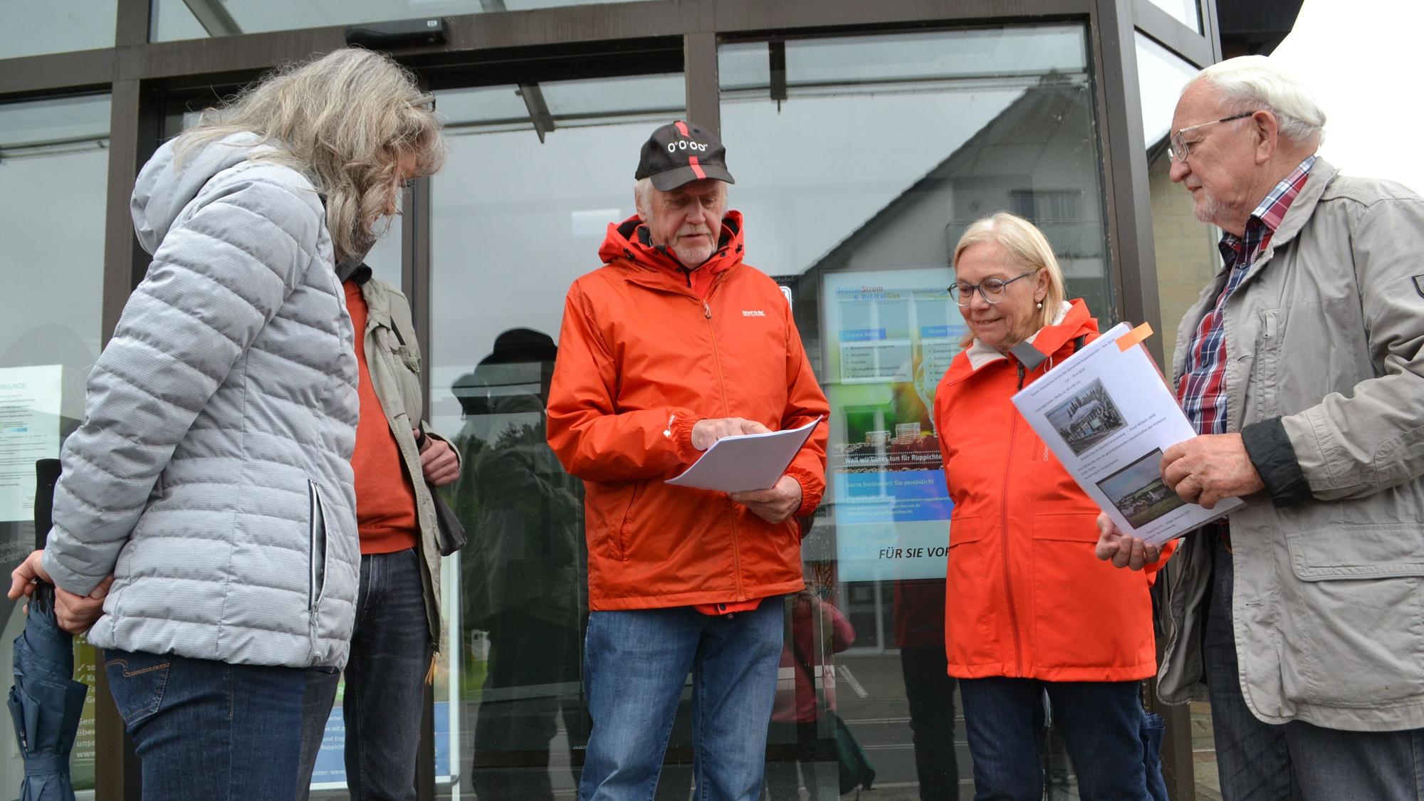 Männer und Frauen in wetterfester Kleidung vor einem verglasten Gebäudeeingang.