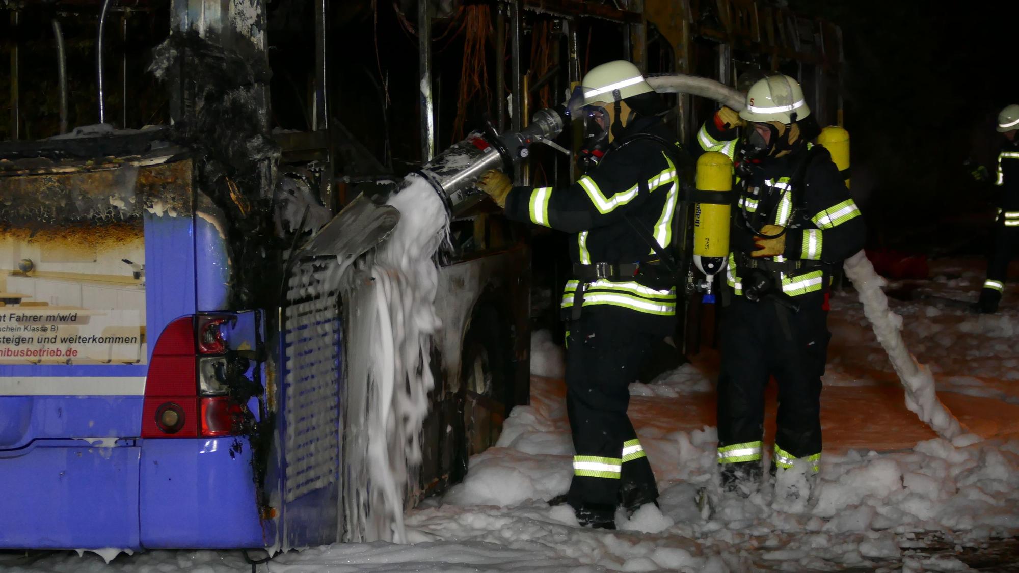 Feuerwehrleute löschen einen Bus mit Schaum.