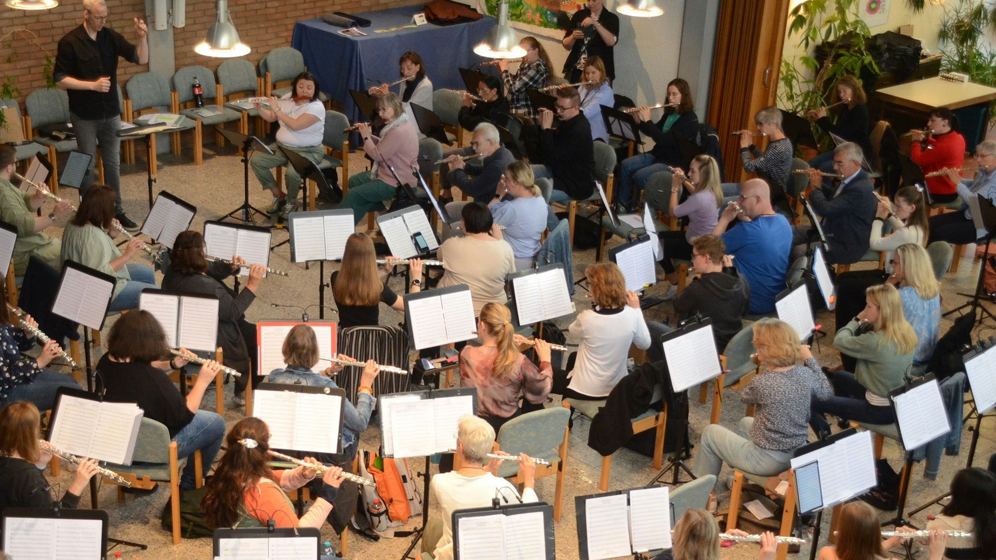 Männer und Frauen spielen Querflöte in einem großen Ensemble. Sie sitzen in ein em großen Halbkreis vor ihren Notenpulten.