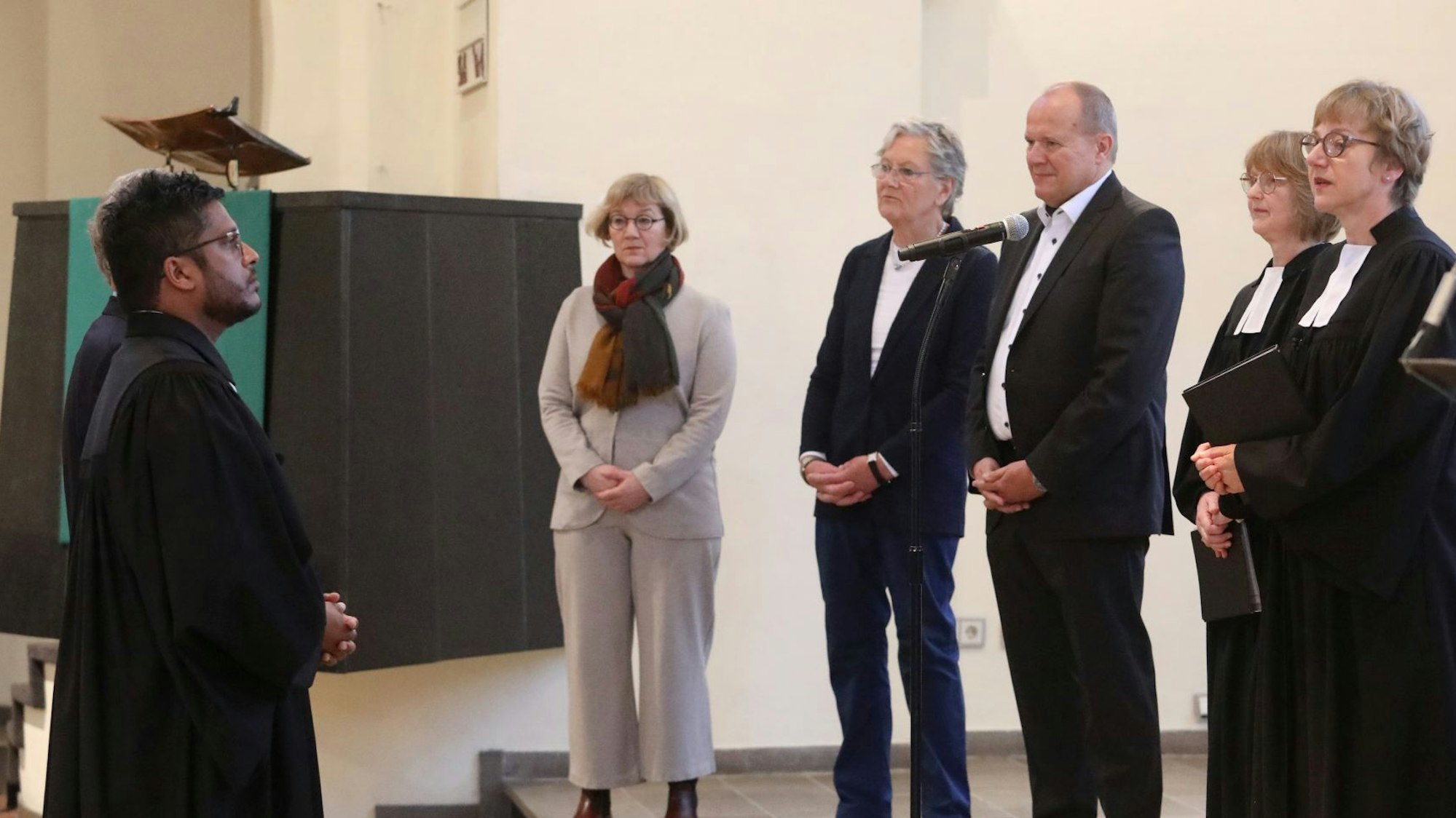 Eine Gruppe von Männern und Frauen, darunter zwei Pfarrerinnen, stehen sich gegenüber, im Hintergrund die Kanzel der Erlöserkirche.