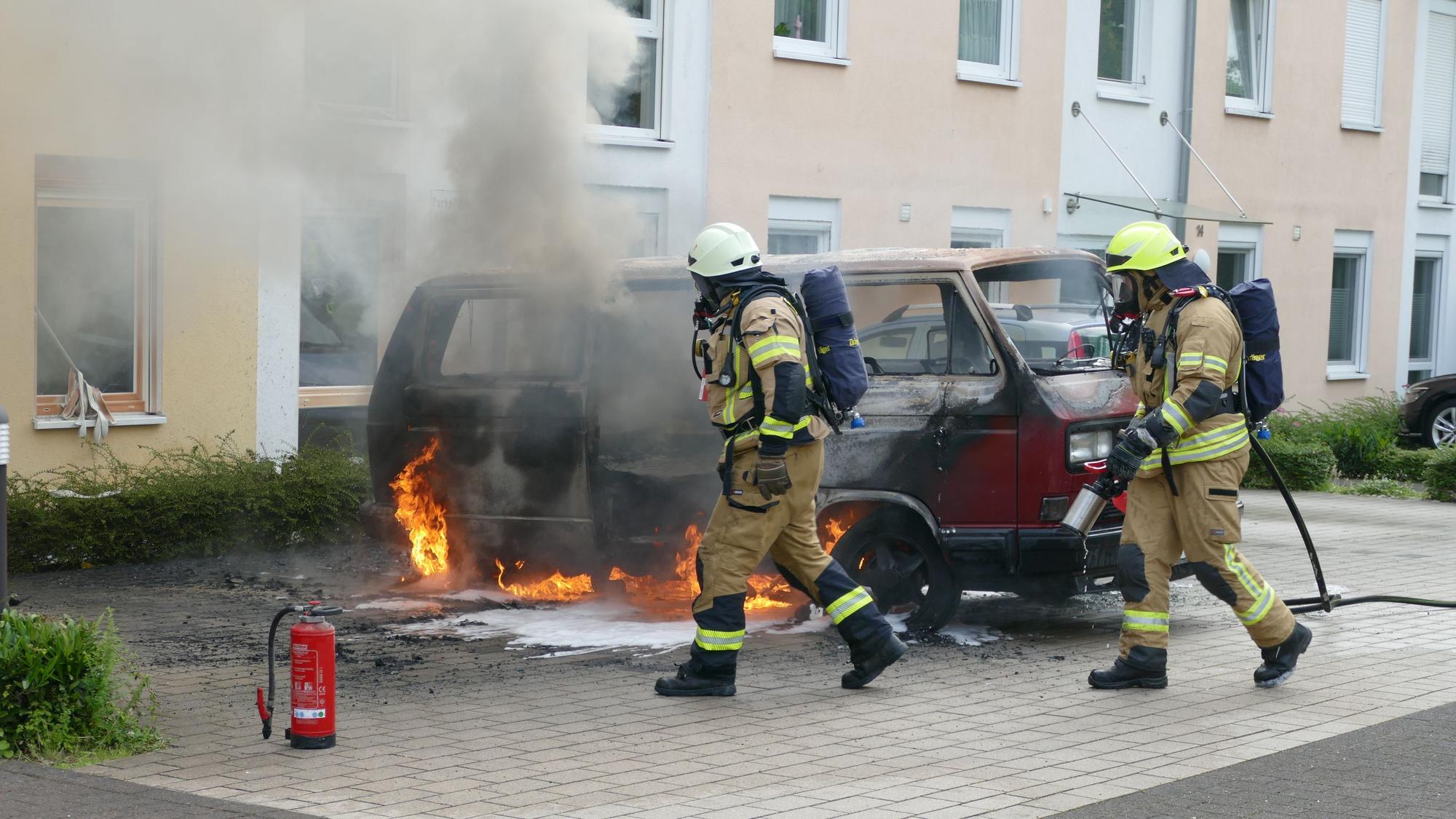 Feuerwehrleute vor einem brennenden Auto.