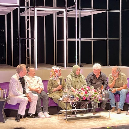 Auf einem langen lila Sofa sitzen (von links nach rechts): Thomas Laue, Stefko Hanushevsky, Meral Sahin, Ismet Büyük, Ayfer Sentürl Demir, Kutlu Yurtseven und Stefan Bachmann