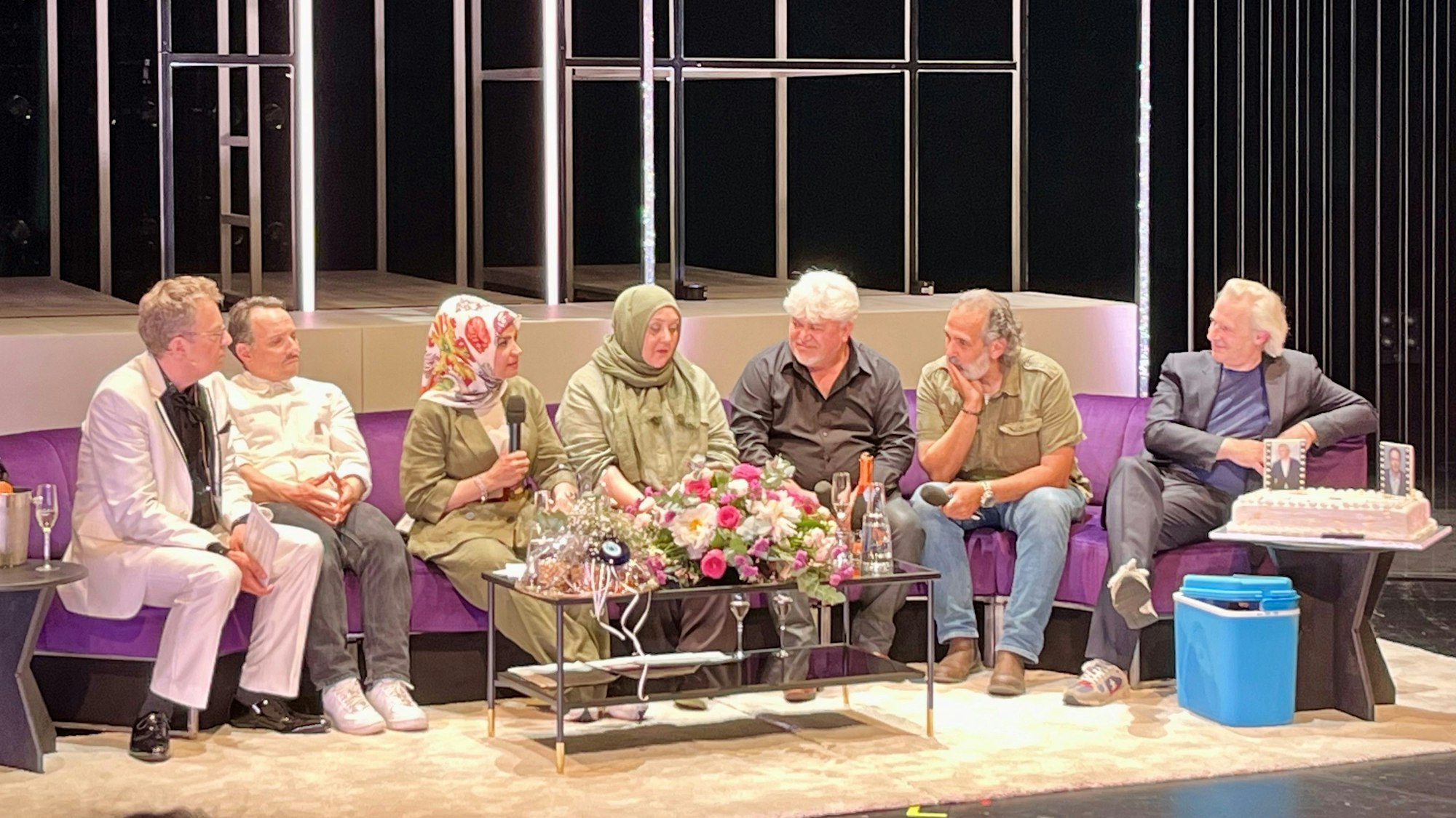 Auf einem langen lila Sofa sitzen (von links nach rechts): Thomas Laue, Stefko Hanushevsky, Meral Sahin, Ismet Büyük, Ayfer Sentürl Demir, Kutlu Yurtseven und Stefan Bachmann