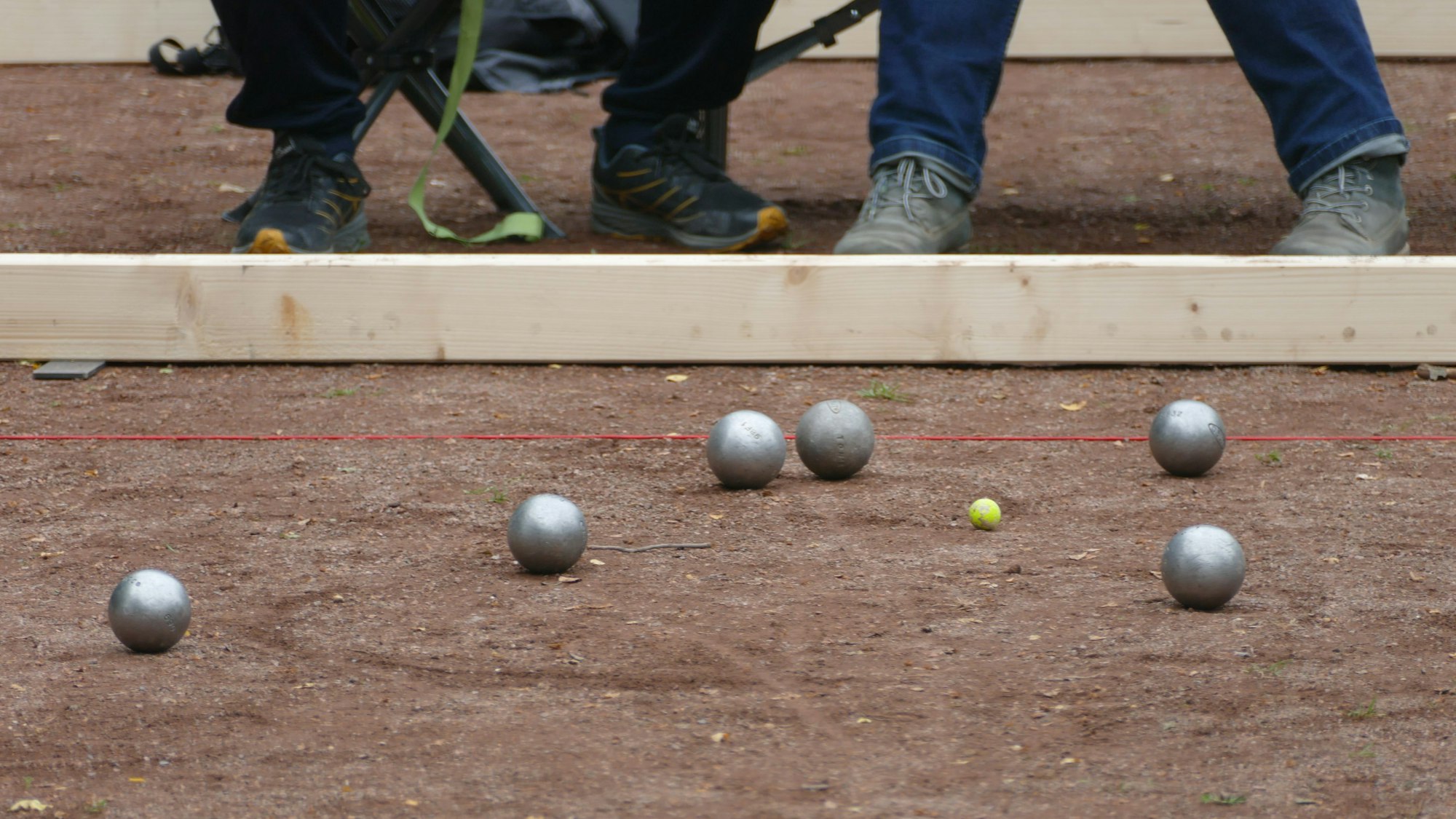 Sechs Boulekugeln auf einer Boulebahn. Eine kleine gelbe Kugel ist das Ziel, das sogenannte Schweinchen.