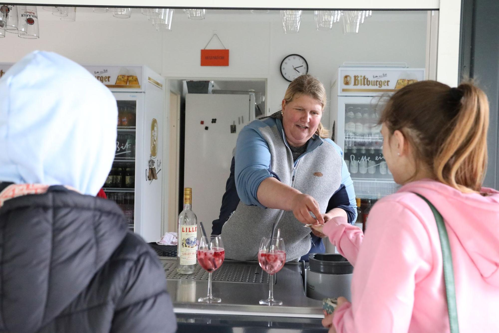 Eine Frau an einer Theke bedient zwei Kunden.