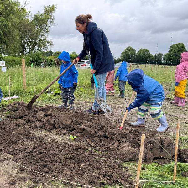 Auf dem Bild ist eine Waldpädagogin zu sehen, die Kita-Kindern zeigt, wie Bohnen gepflanzt werden.