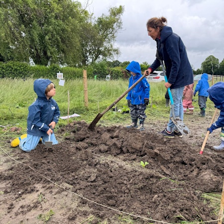 Auf dem Bild ist eine Waldpädagogin zu sehen, die Kita-Kindern zeigt, wie Bohnen gepflanzt werden.