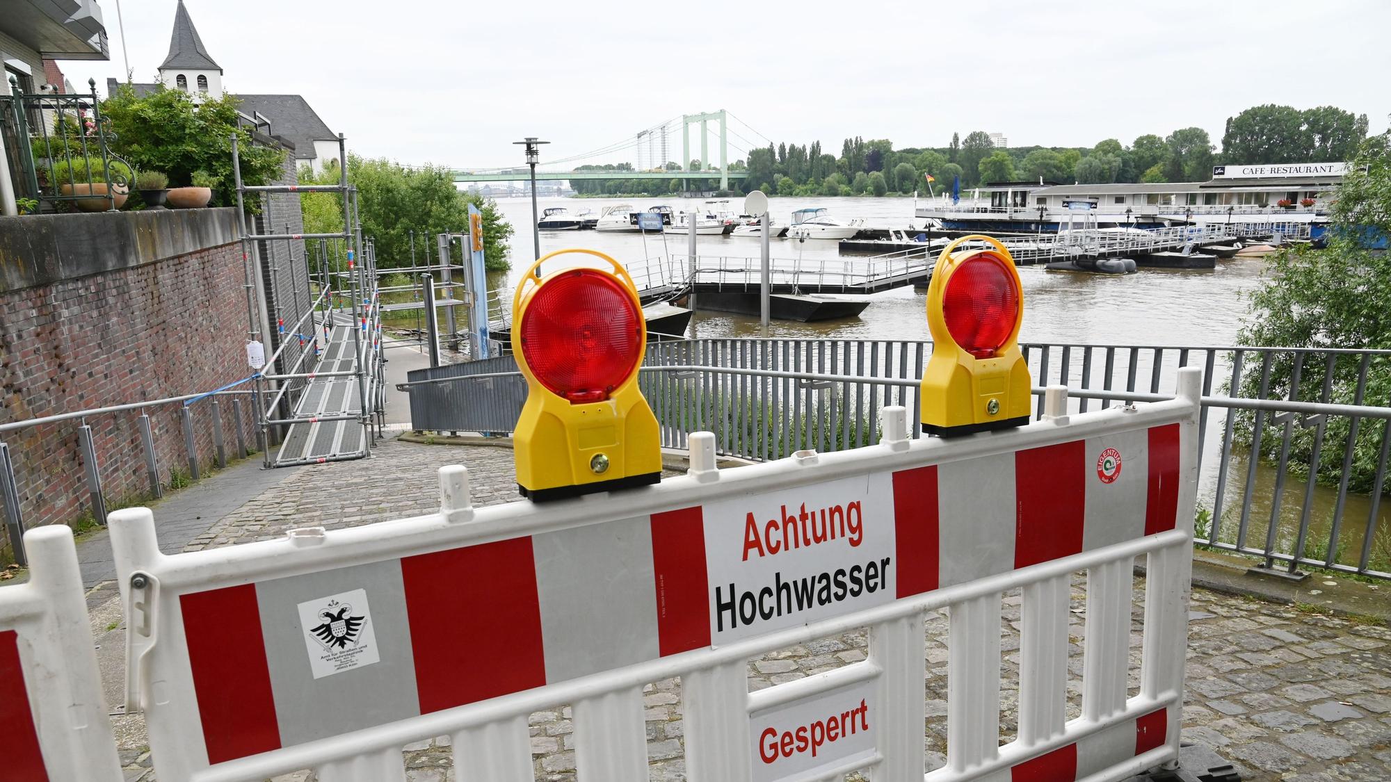 Ein Weg ist mit dem Schild „Achtung Hochwasser“ abgesperrt. Im Hintergrund ist der Rhein zu sehen.