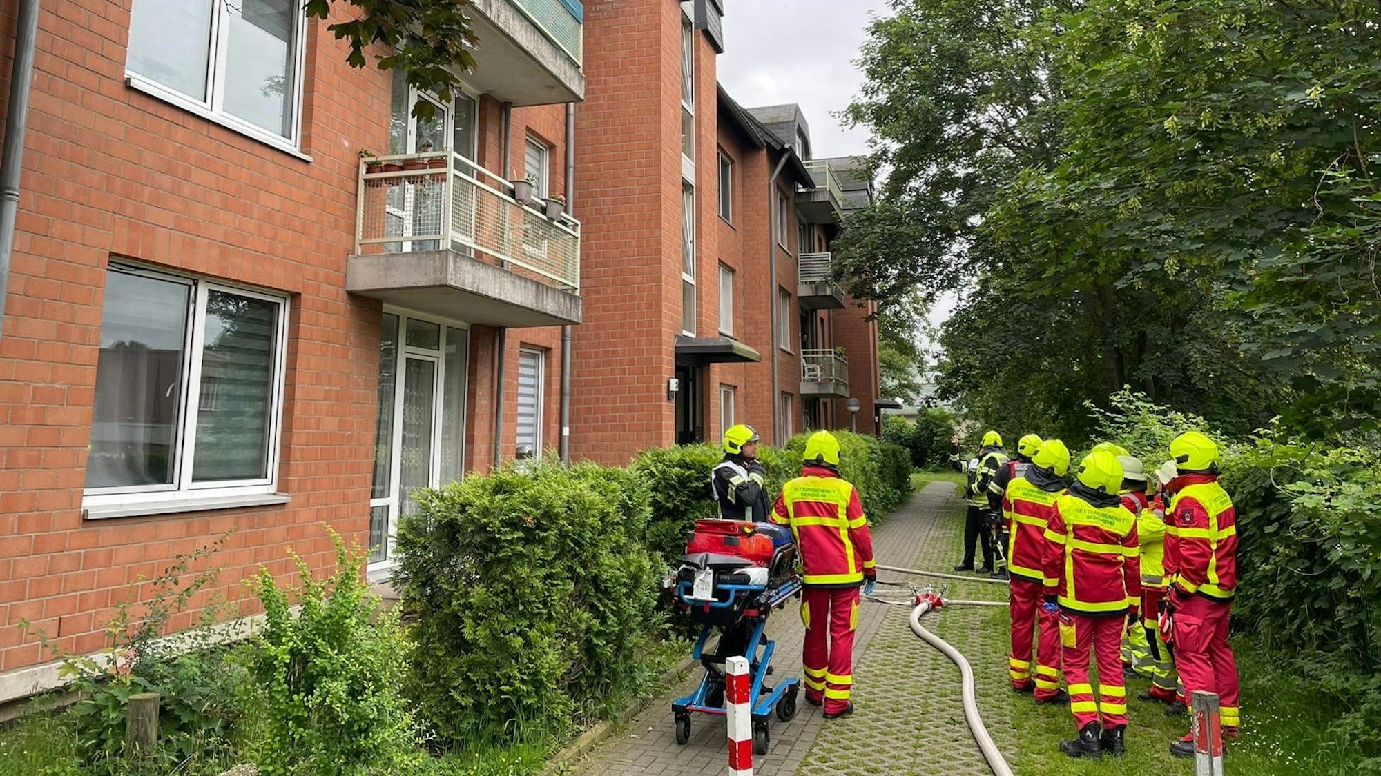 Feuerwehrleute stehen vor einem Wohnhaus in Bergheim, vor ihnen auf dem Boden liegt ein Löschschlauch.