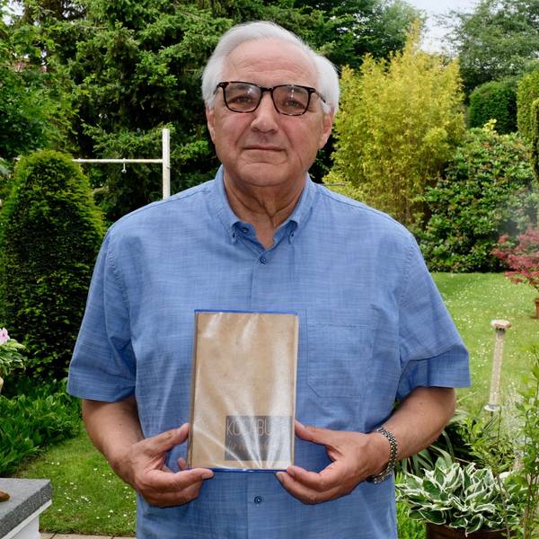Zu sehen ist ein Mann, der ein Kochbuch hält, in einem Garten.