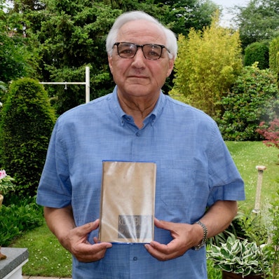 Zu sehen ist ein Mann, der ein Kochbuch hält, in einem Garten.