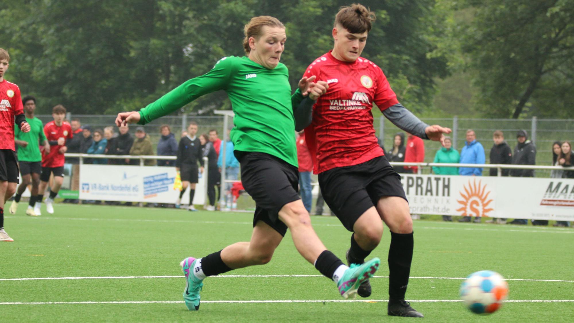 Der Fußballer Luke Gossing (l.) trägt ein grünes Trikot und wird von einem Gegenspieler beim Schuss bedrängt.
