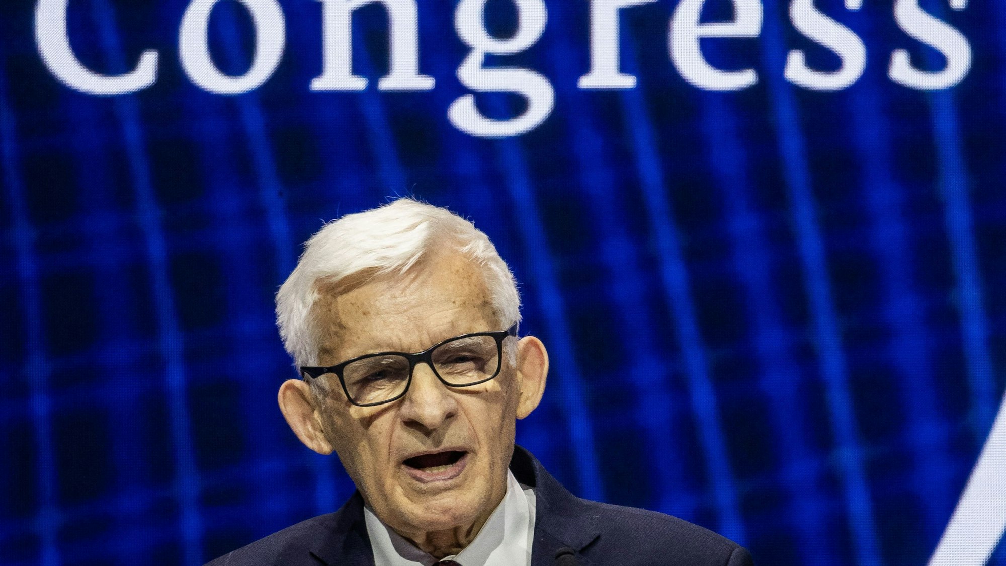 Der frühere Premierminister von Polen, Jerzy Buzek, ist mit 82 Jahren das derzeit älteste Mitglied des Europäischen Parlaments. Im Bild ist er im Porträt auf einer Veranstaltung zu sehen mit schwarzer Brille und weißem Kurzhaarschnitt.