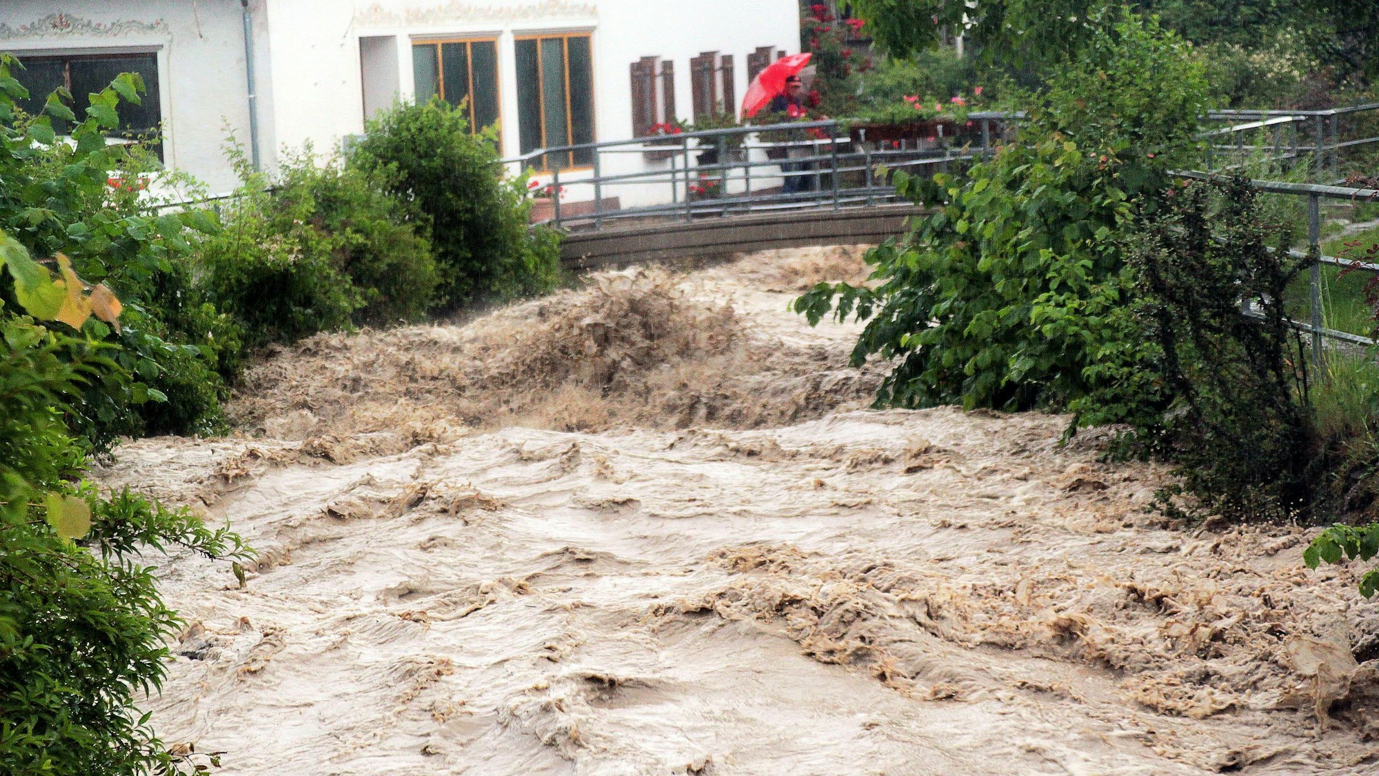 Ein Passant steht auf einer Brücke über den Auerbach im Ortsteil Au im Landkreis Rosenheim. Der Bach entwickelte sich am Montag nach Starkregen zu einer reißenden Flut.