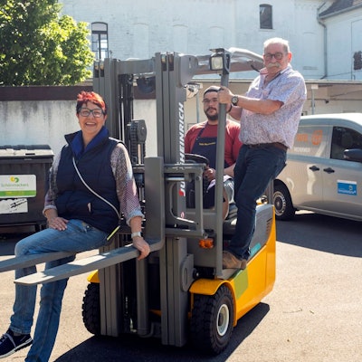 Manuela Pütz, Fahrer Tim Achnitz und Wolfgang Weilerswist posieren auf einem Gabelstapler fürs Foto.