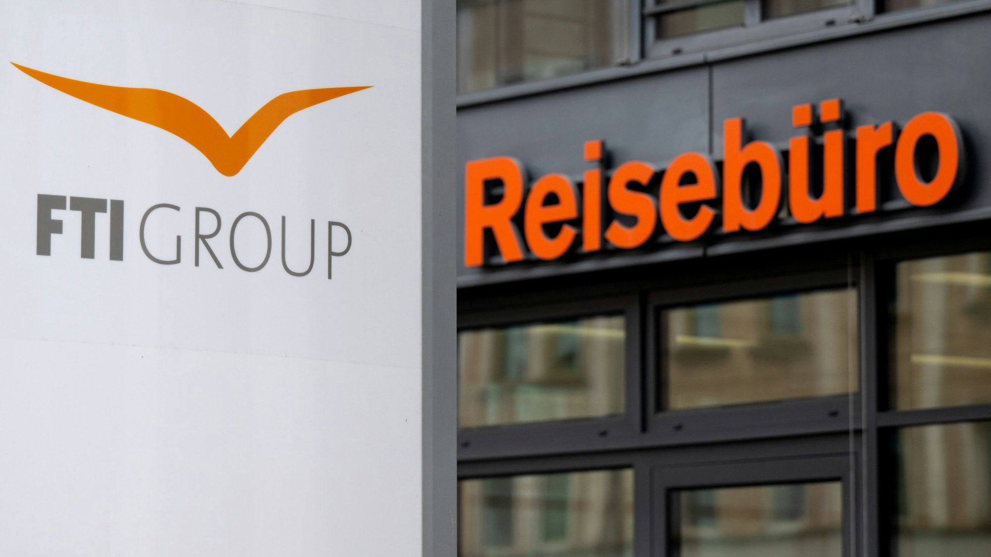 Das Logo des Reiseveranstalter FTI (FTI Group) steht an der Firmenzentrale vor einem Reisebüro.