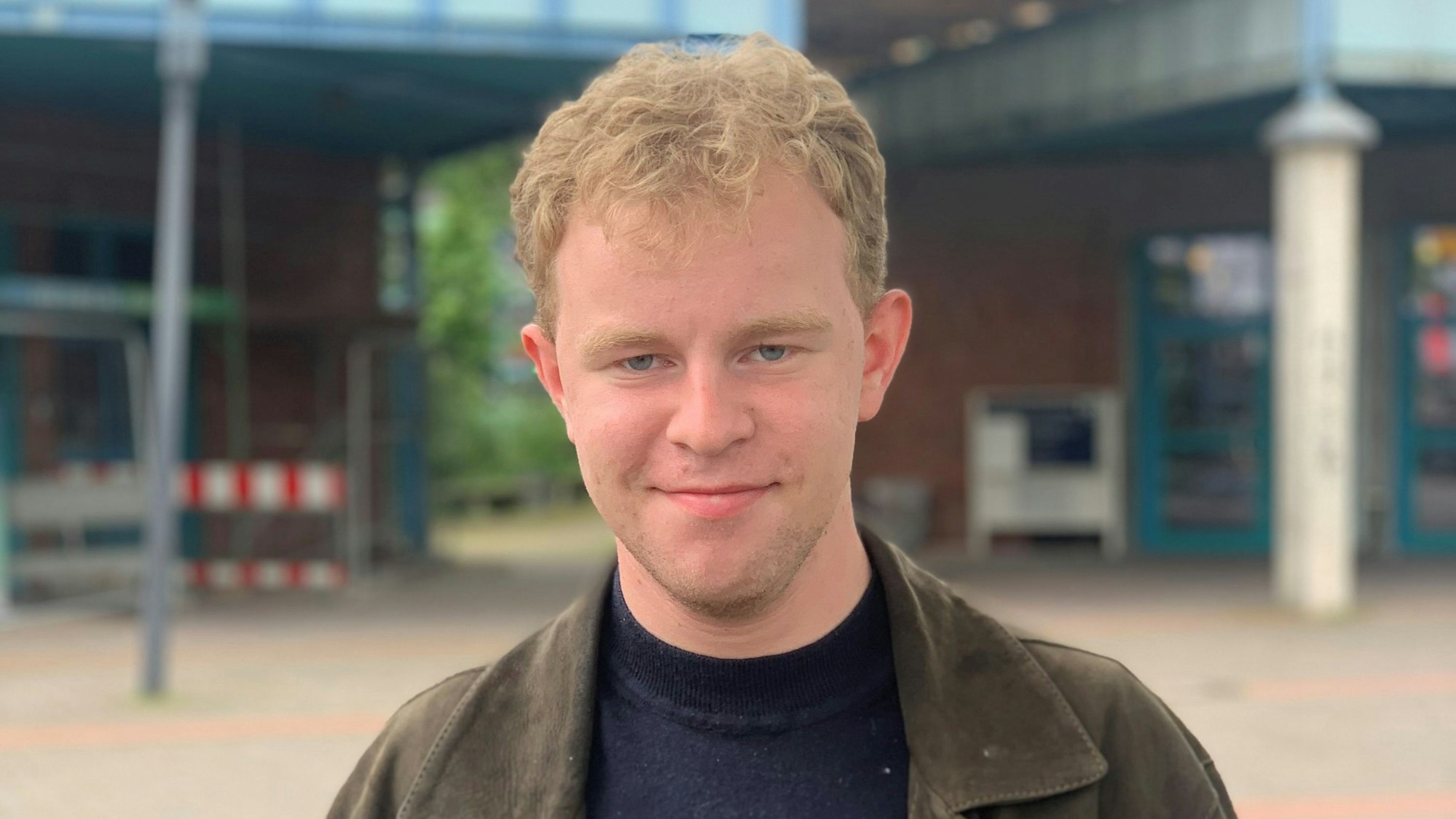 Ein junger Mann steht vor einem Schulgebäude und lächelt.