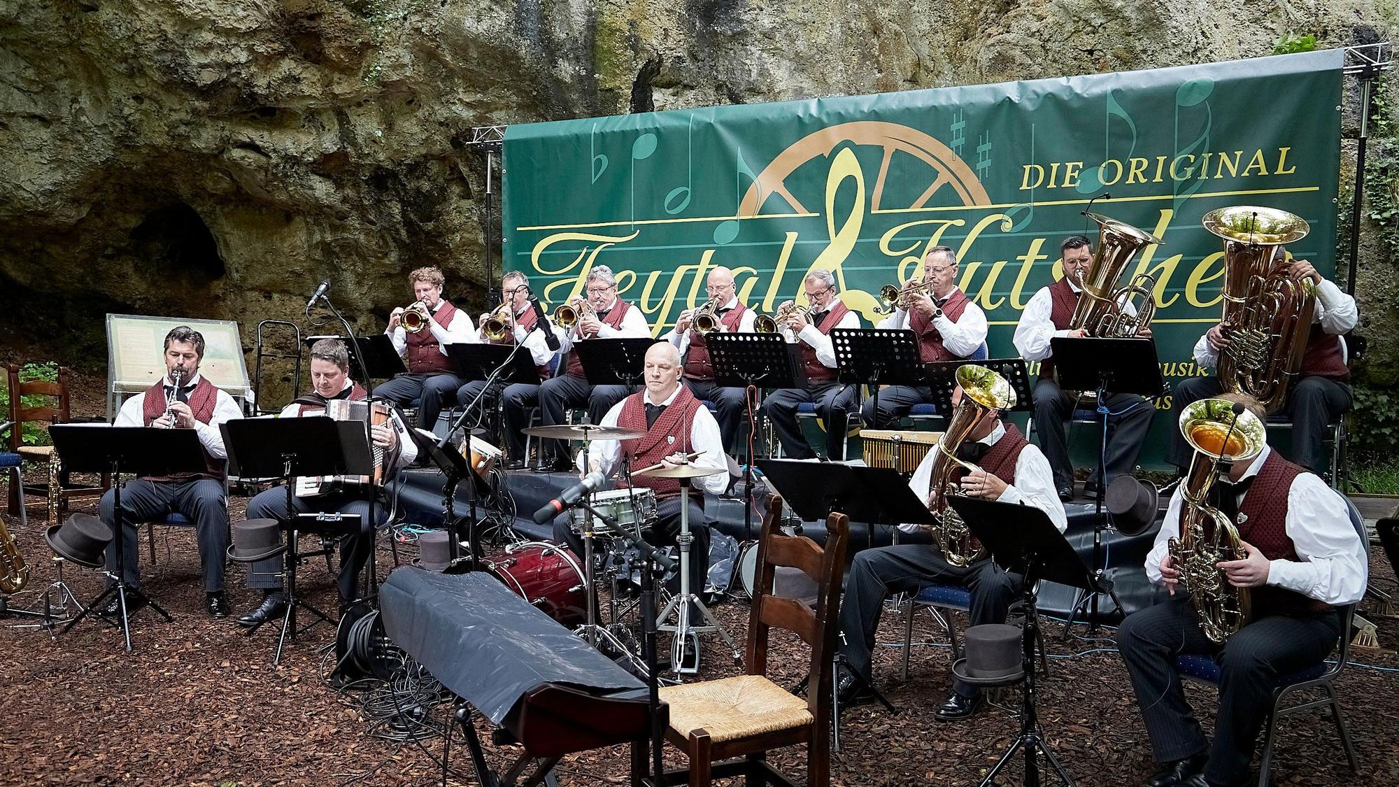 Die Musikanten der Feytal-Kutscher sitzen vor der Kakushöhle in Mechernich auf ihren Stühlen und spielen auf ihren Blasinstrumenten.