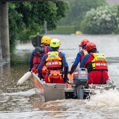 DLRG-Retter fahren mit einem Motorboot auf einer überfluteten Straße.
