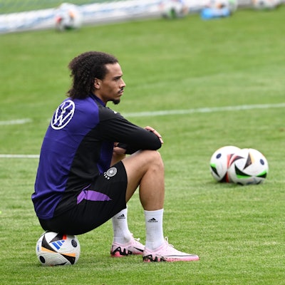 Leroy Sané sitzt auf einem Ball und beobachtet die Spieler beim Training.