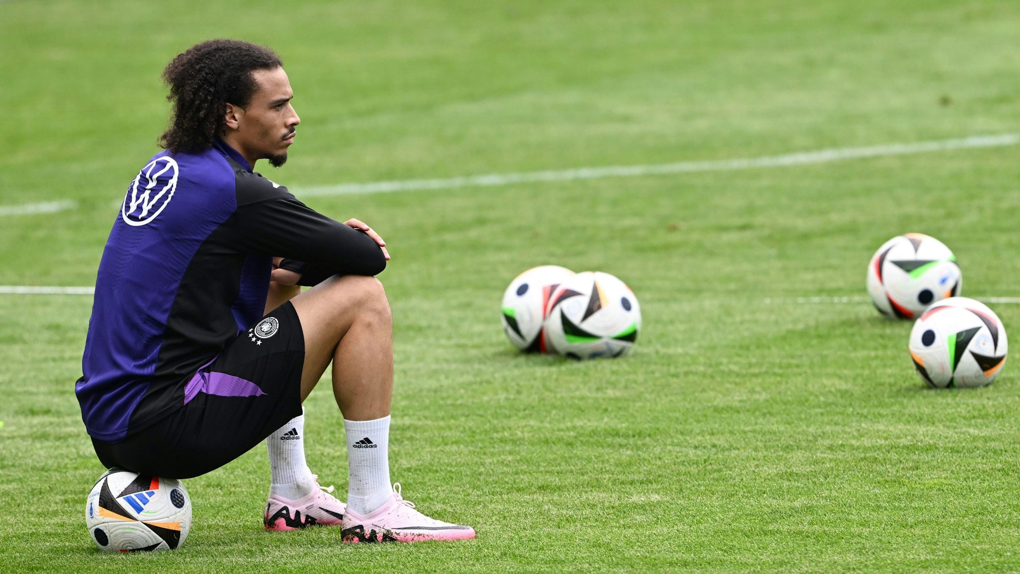 Leroy Sané sitzt auf einem Ball und beobachtet die Spieler beim Training.