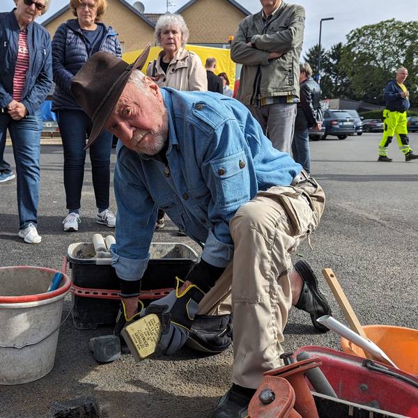 Der Künstler Gunter Demnig lässt den Stolperstein in den Asphalt ein. Neben ihn ein Eimer mit Zement.